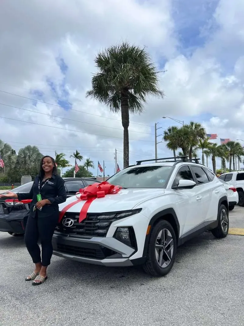 A customer presenting a new white Hyundai Tucson finished with a red delivery bow