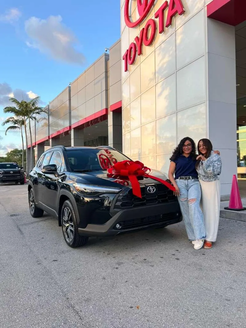Two customers celebrating together beside a new black Toyota Corolla Cross with a red delivery bow