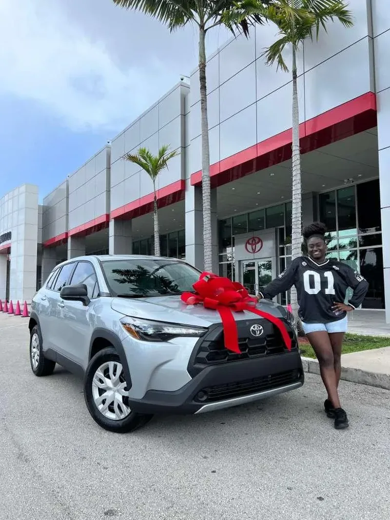 A customer standing beside her new silver Toyota Corolla Cross, finished with a red delivery bow