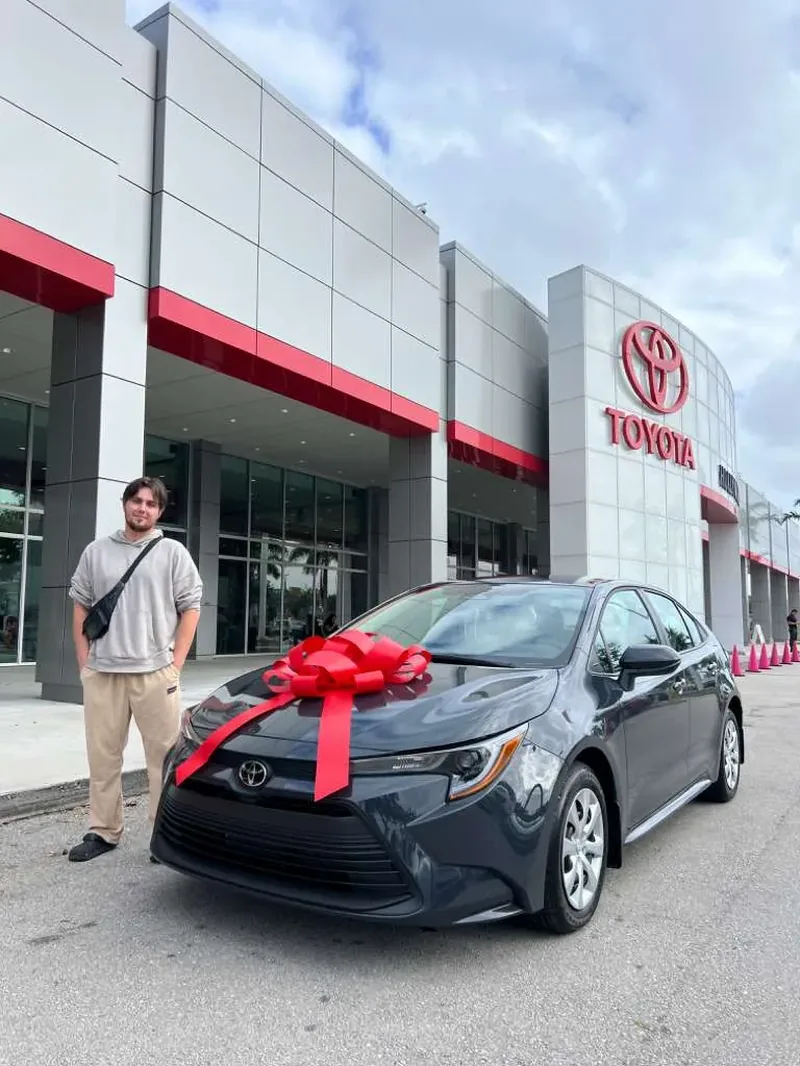 A customer standing beside his new grey Toyota Corolla with a red delivery bow